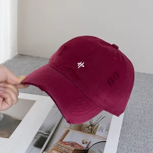 Detail of distressed burgundy baseball cap with white embroidery and frayed edges