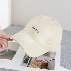 Detailed embroidery of Smile text on distressed beige cotton baseball cap with torn details