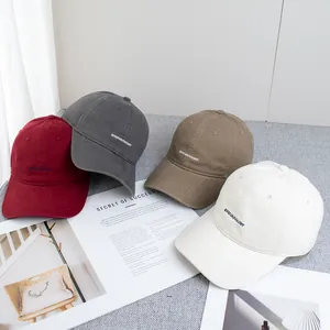 Flat lay of cotton baseball caps in burgundy, grey, khaki and cream with letter embroidery