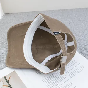 Khaki cotton baseball cap with adjustable metal buckle on a minimalist book background