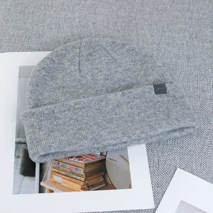 Detail of grey wool beanie with AIM leather brand tag on a textured magazine background