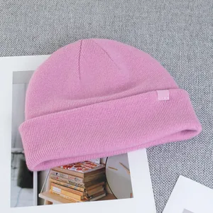 Detail of pink wool beanie showing fine knit texture and decorative brand logo tag