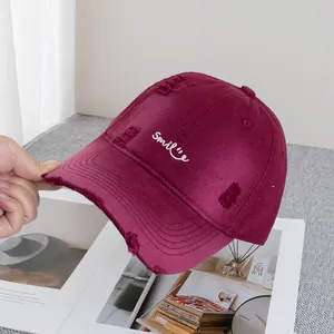 Close-up of distressed burgundy baseball cap featuring white smile embroidery and vintage tears