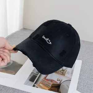 Close-up of black baseball cap with white Smile embroidery and distressed ripped details