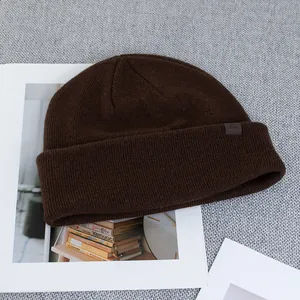 Detail of dark brown knitted wool beanie with thick cuff and side logo patch on grey fabric