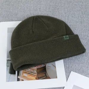 Detail of dark green wool knit beanie with ribbed texture and woven logo patch on cuff