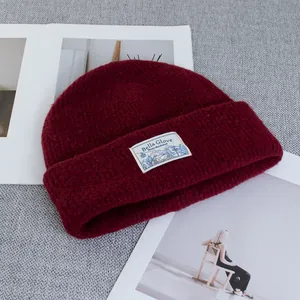 Close-up of deep red wool knit beanie with winter label on textured background