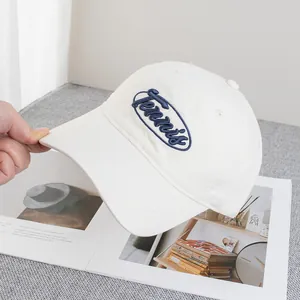 Gros plan sur la broderie bleue 'Tennis' d'une casquette en coton blanc cassé