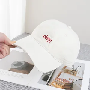 Close-up of beige canvas baseball cap featuring red .okey! embroidery and worn brim details