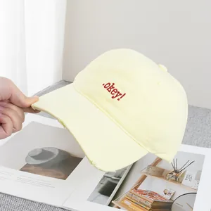 Detail of light yellow cotton baseball cap featuring red .okey! embroidery and frayed brim