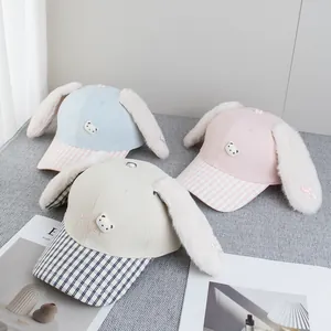 Detailed view of plush rabbit ear baseball caps in blue, pink, and beige with bear embroidery