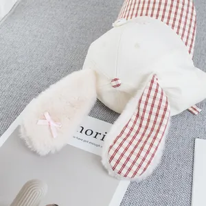 Detailed view of plush rabbit ears with pink bow and red plaid pattern on a beige cap