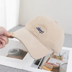 Close-up of embroidered .okay! text and distressed brim on beige cotton baseball cap