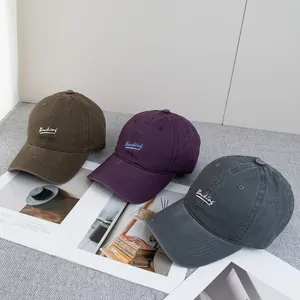 Three embroidered cotton baseball caps in green, purple and gray on a stylish background
