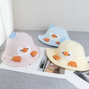 Three colorful baby penguin bucket hats in pink, light blue and yellow on a magazine