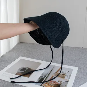Dettaglio del cappello di paglia nero che mostra la trama intrecciata e i laccetti decorativi