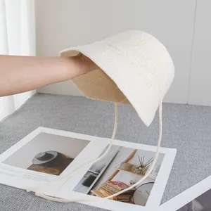 Dettaglio del cappello da sole in paglia color crema con texture traspirante e lacci lunghi