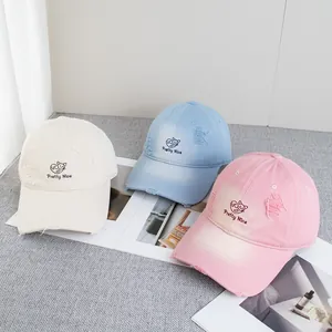 Detailed view of distressed baseball caps in beige, blue, and pink with cat embroidery
