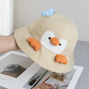 Detail of khaki cotton bucket hat featuring a 3D penguin face and blue fish ornament