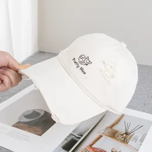 Detail of embroidered cat and distressed holes on off-white canvas baseball cap