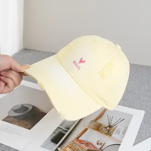 Detail of distressed brim and pink heart embroidery on a soft yellow baseball cap