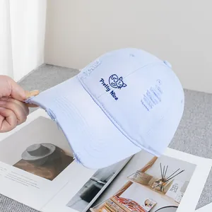 Detailed close-up of blue distressed denim cap with cat embroidery and frayed holes