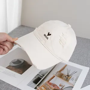 Detail of beige baseball cap with distressed brim and black heart embroidery