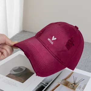 Close-up of wine red baseball cap featuring distressed holes and hello heart embroidery