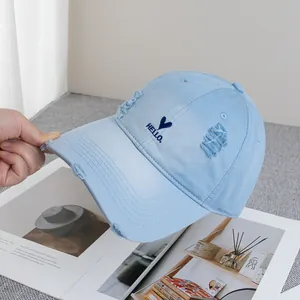 Detailed view of light blue denim baseball cap with distressed holes and heart embroidery