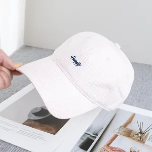 Dettaglio del cappellino a quadretti rosa con ricamo Happy blu e simbolo di una faccina