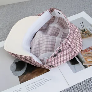 Pink plaid newsboy cap with cat embroidery and interior lining shown on a magazine