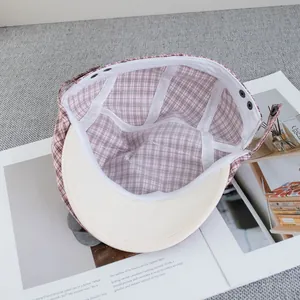 Detail of pink plaid newsboy cap interior showing white lining and snap buckle
