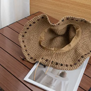 Cappello da sole in paglia intrecciata a mano con perline e sottogola su tavolo in legno