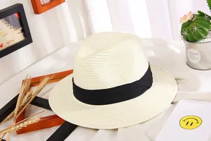 Detail of a beige woven straw sun hat featuring a classic black ribbon and wide brim