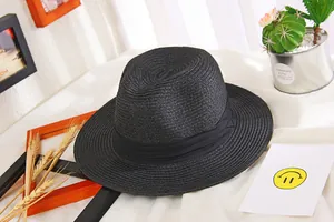 Black wide-brim straw sun hat with decorative band on a flat lay leisure background