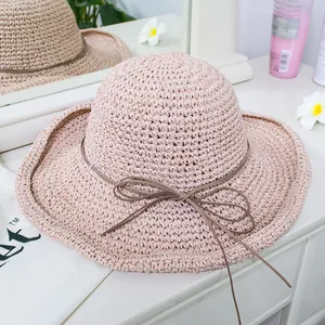 Detail of light pink woven straw hat with thin brown decorative bow tie on a white table