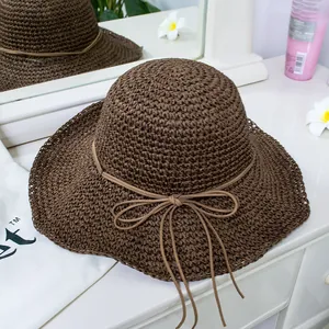 Detail of dark brown straw sun hat with wavy brim and bow next to a white dust bag