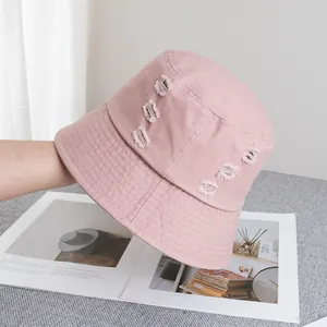 Détail du chapeau bob en coton rose pâle avec trous usés et bord large de style décontracté
