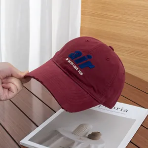 Detail of distressed burgundy baseball cap with blue air letter embroidery and torn brim