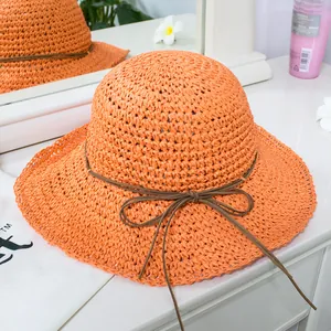 Detail of a bright orange woven straw hat with a slim brown leather bow decoration