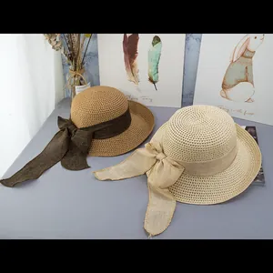 Dettaglio di cappelli di paglia a tesa larga con lunghi fiocchi di nastro su sfondo grigio