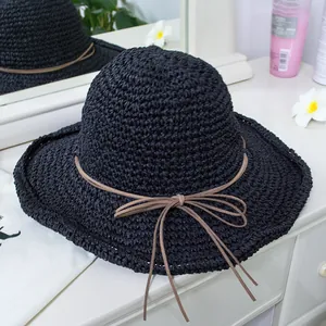 Close-up of black woven straw hat with a slim brown bow detail and wavy sun brim