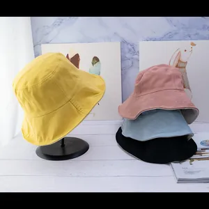 Detail view of cotton bucket hats in yellow, pink, blue and black in a minimalist setting