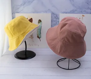 Detailed view of double-sided cotton bucket hats in yellow and pink on metal stands