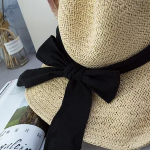 Close-up of beige straw sun hat featuring a large black fabric bow and natural woven texture