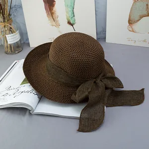 Primo piano di un cappello di paglia marrone con fiocco in tessuto su sfondo minimalista