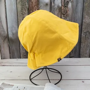 Detailed view of yellow cotton sun hat with a brown decorative label on a black metal stand