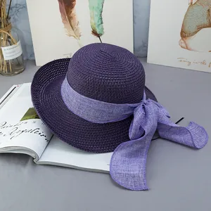 Dettaglio di cappello di paglia viola con fiocco in lino chiaro su sfondo grigio estetico