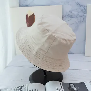 Detail shot of a beige cotton bucket hat with parallel brim stitching on a black stand