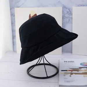 Close-up of a black canvas bucket hat with reinforced stitching on a metal display stand